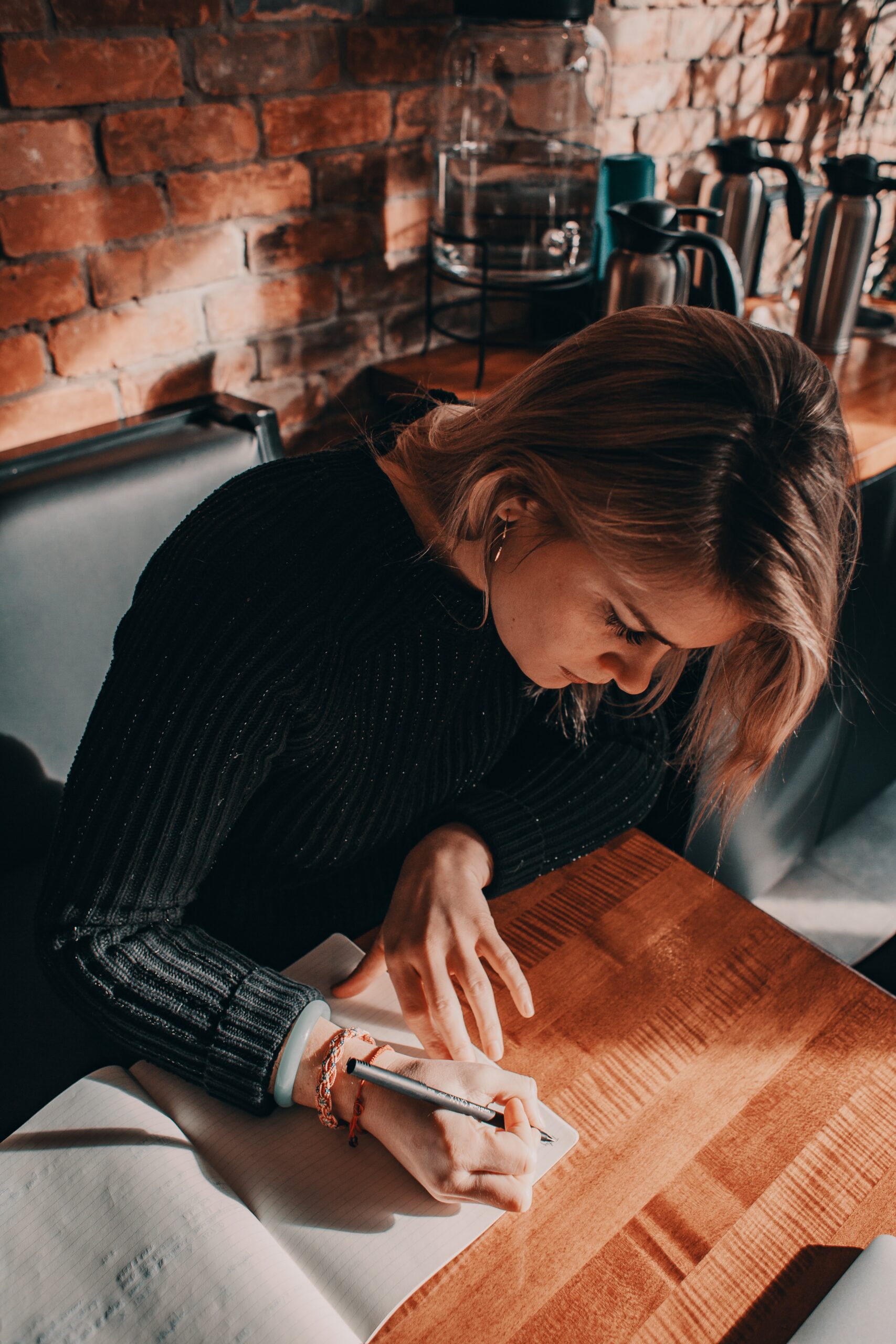 woman with dark blonde hair writing in a journal on a wooden desk